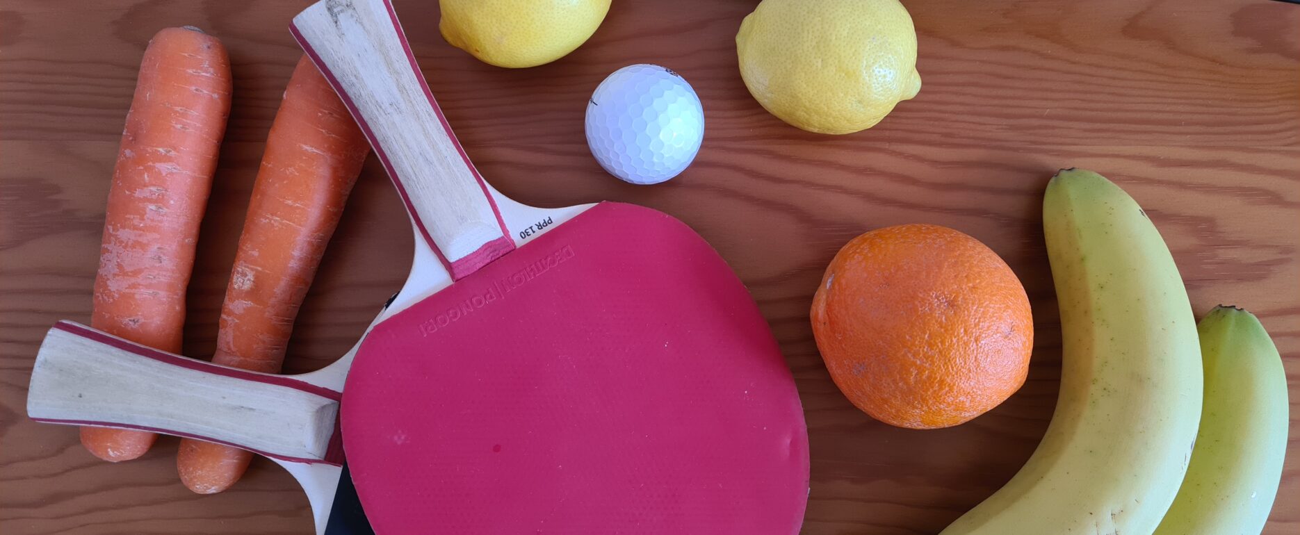 Foto beschreibt Sachverhalt des Folgetextes: Gesund ernähren und Sport treiben. Zu sehen sind darauf: Karotten, Zitronen, Orangen und Bananen. Tischtennischläger, Squashschläger, Golfball.